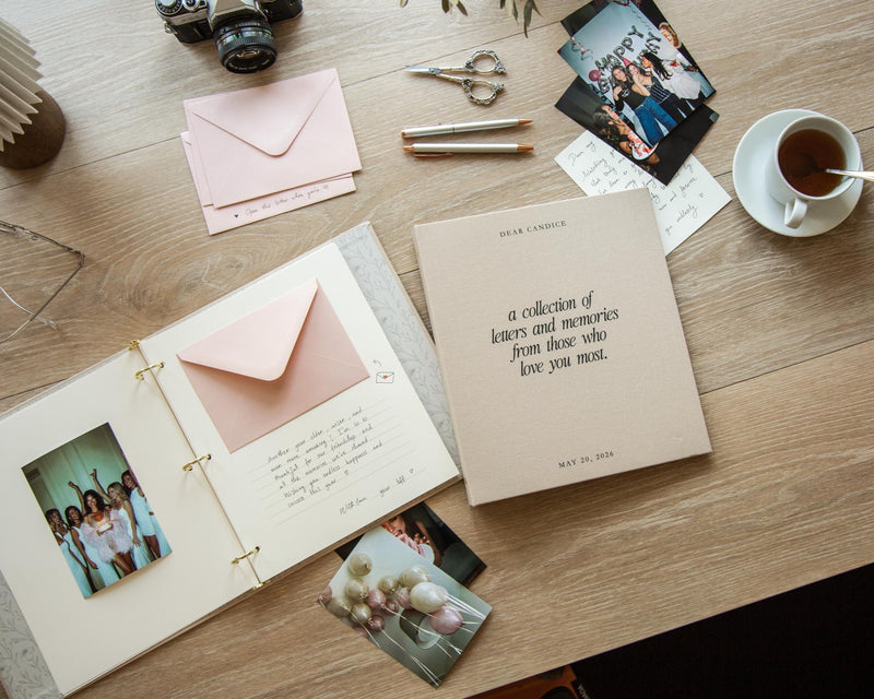 May include: A beige memory book with the text "DEAR CANDICE, a collection of letters and memories from those who love you most, MAY 20, 2026" on the cover, displayed open with a pink envelope, handwritten notes, and photographs inside.